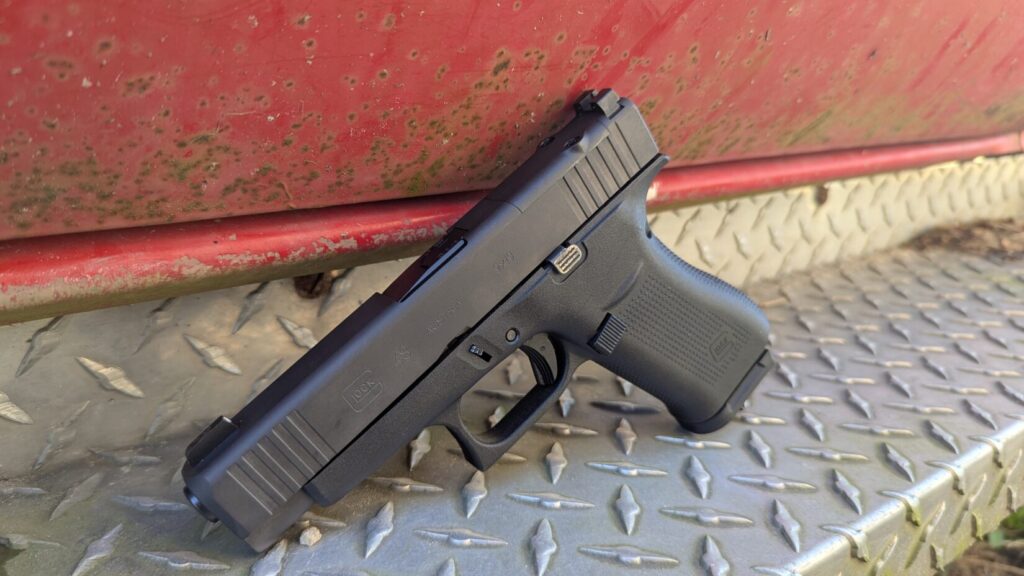 A Glock 48 pistol resting on a diamond-plate metal step next to a red vehicle.