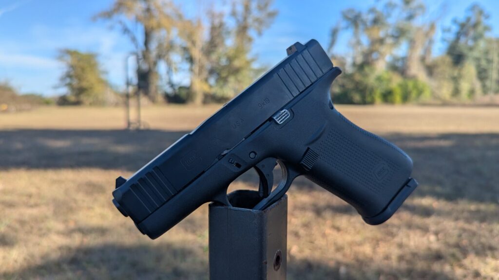 Profile view of a Glock 43X pistol balanced on a metal post outdoors.