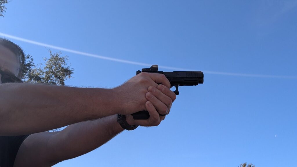 Side view of a person in a shooting stance holding a Glock 17 Gen 6 against a clear blue sky.