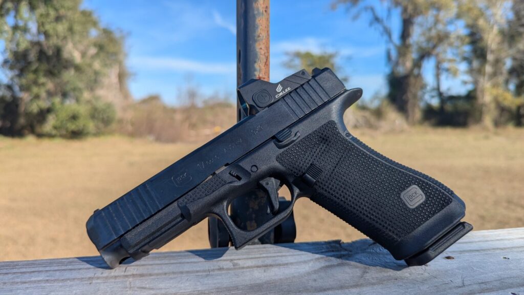 Perspective view of a Glock 17 Gen 6 on a wooden rail, showing the front serrations and optic mounting.