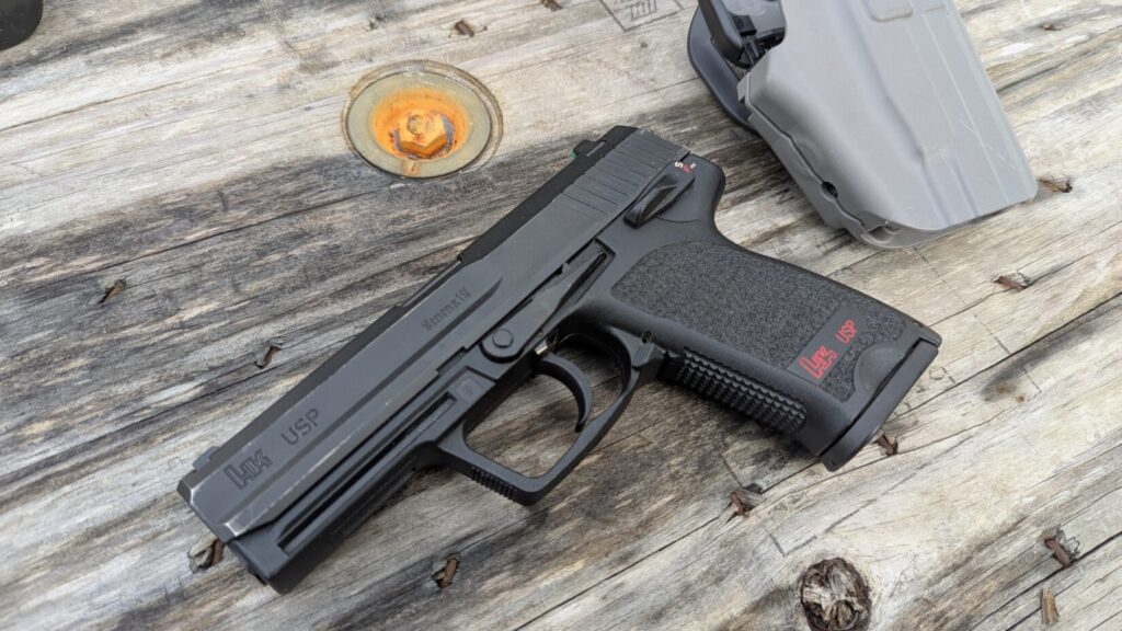 An overhead shot of the HK USP 9mm pistol positioned next to its gray tactical holster.