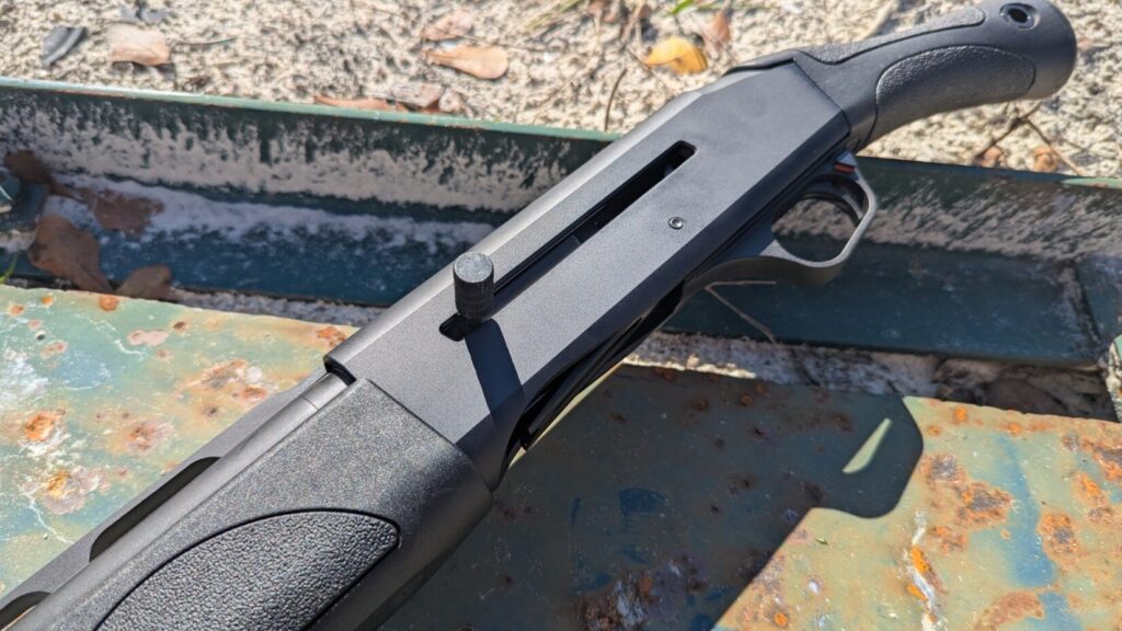 A close-up, high-angle view of the IWI Mafteah's receiver and grip, highlighting the oversized charging handle, the trigger guard with the cross-bolt safety engaged, and the textured bird's head grip.