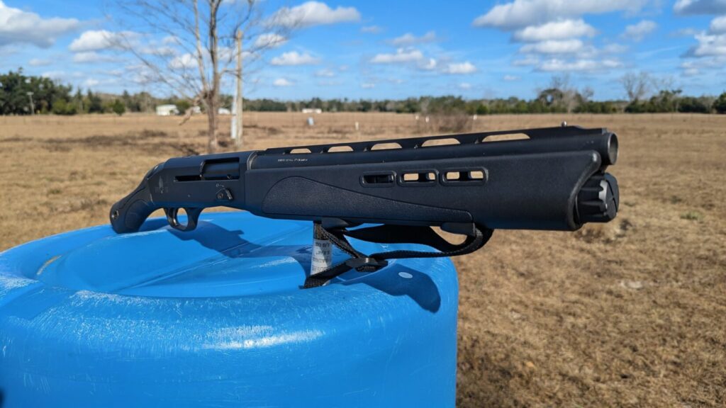 The IWI Mafteah balanced on a blue plastic barrel with a wide-open field and cloudy sky in the background.