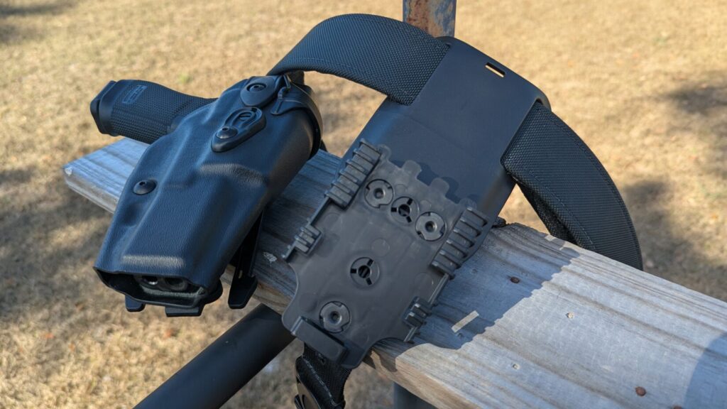 A black duty holster and its mounting receiver plate resting on a wooden rail.