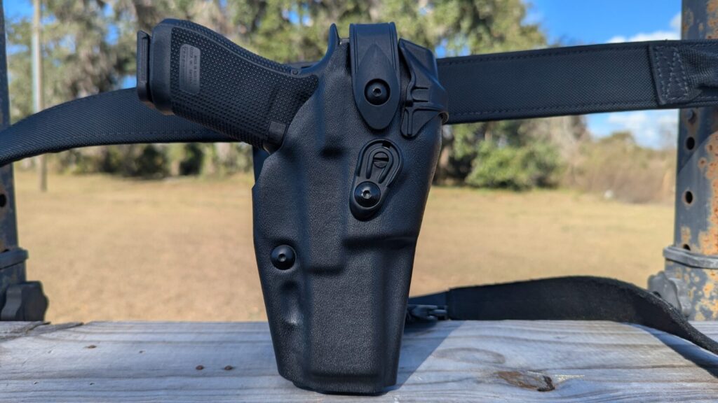 A close-up, rear view of a black handgun equipped with a red dot sight, securely seated inside a tactical holster.