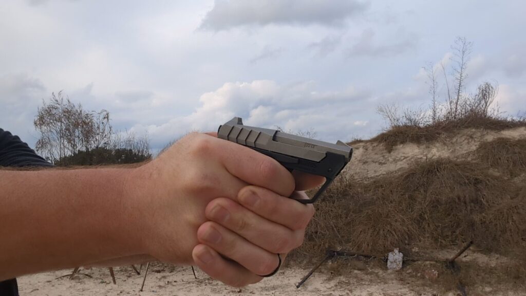 A person holding the Taurus 22TUC in a two-handed grip, ready to fire at an outdoor range.
