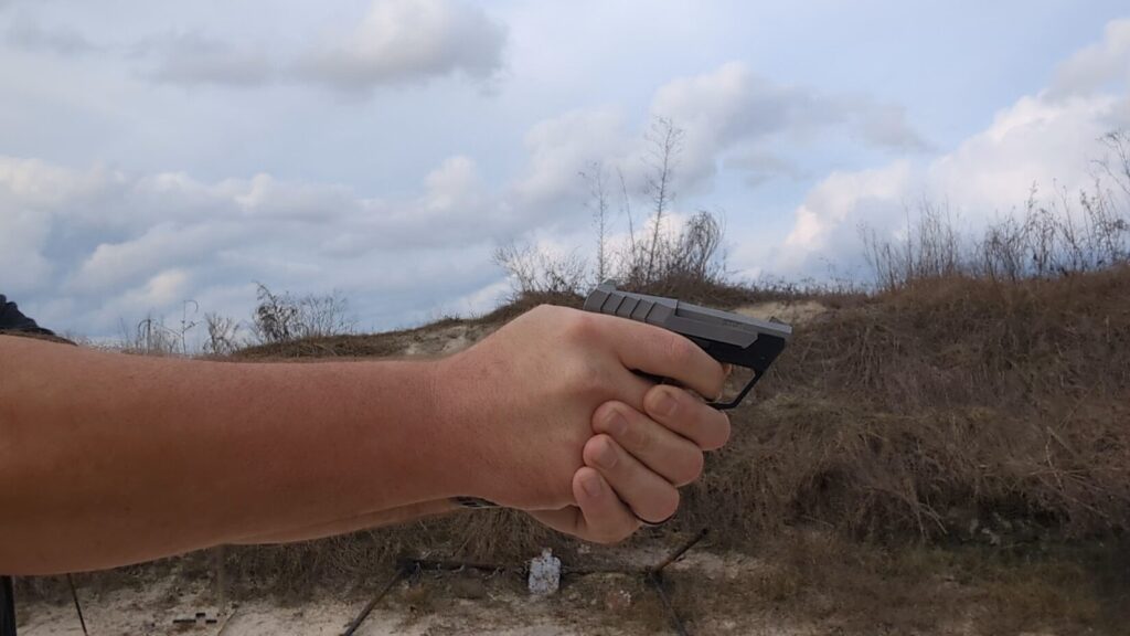 A person holding the Taurus 22TUC in a two-handed grip, ready to fire at an outdoor range.