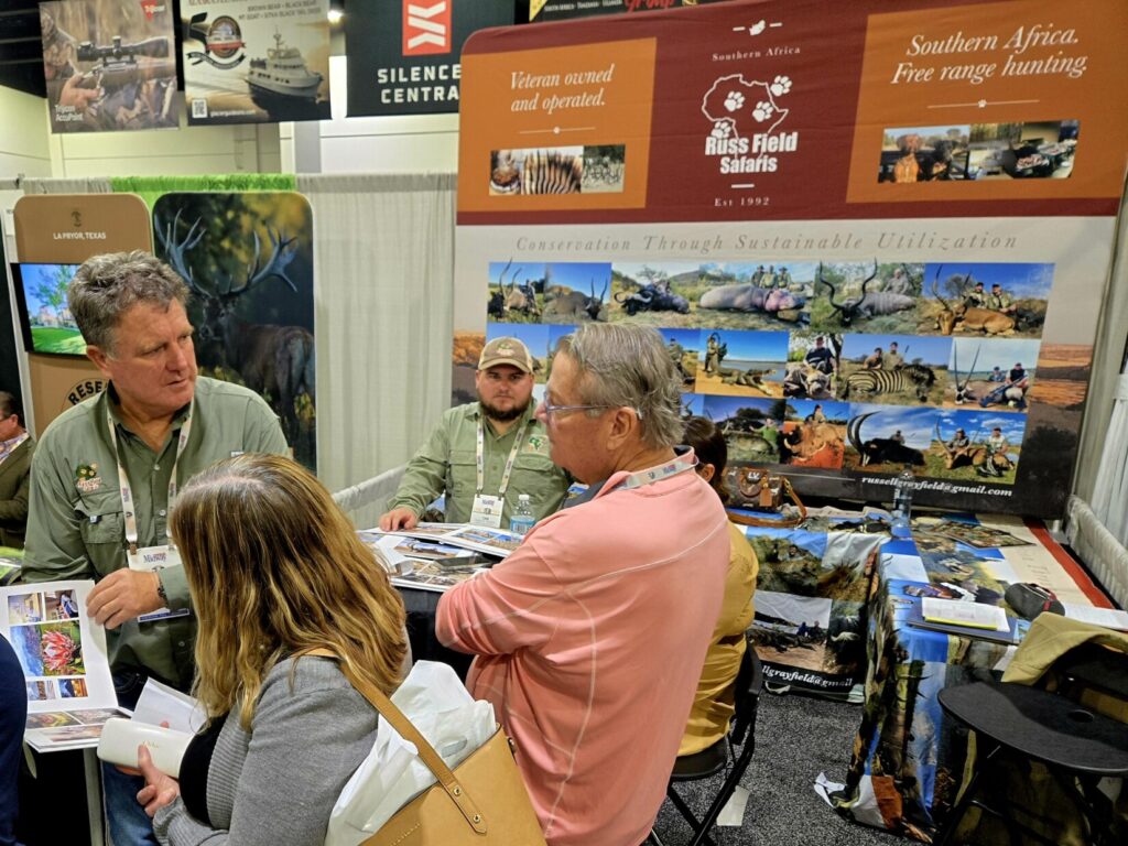 A man showing photos to a couple people in a booth at Dallas Safari Club