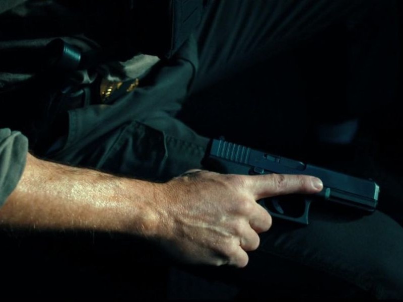 A person with their hand on their leg, holding a pistol.