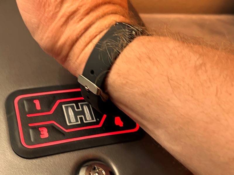 A person holding their wrist (which has a black bracelet) to a safe to open it quickly.