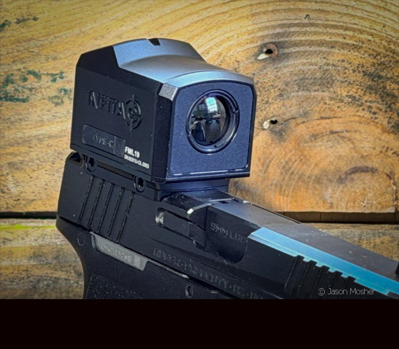 A black thermal optic mounted on top of a black handgun, in front of a wood wall. 