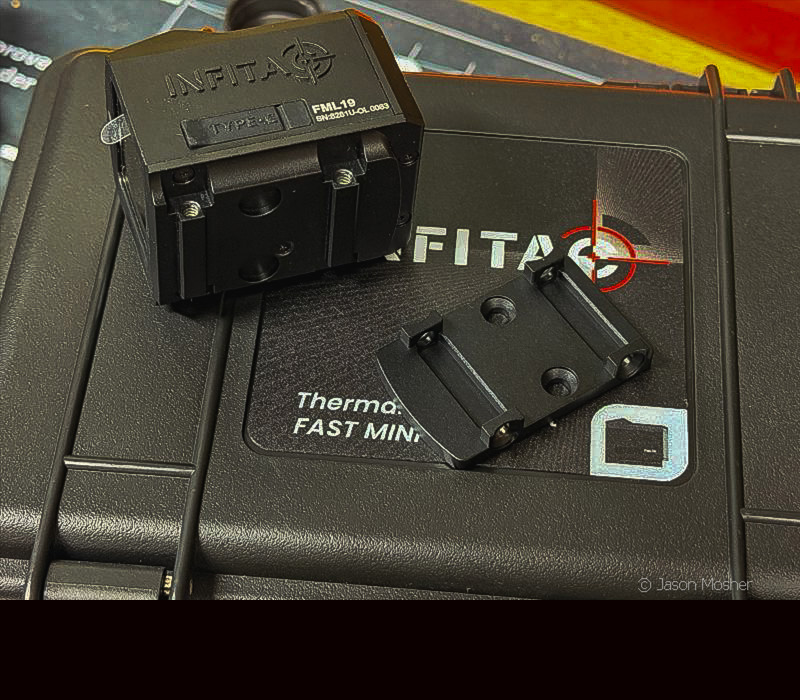 A black thermal optic on it's side with a black mounting plate laying beside it on the box the optic shipped in. 