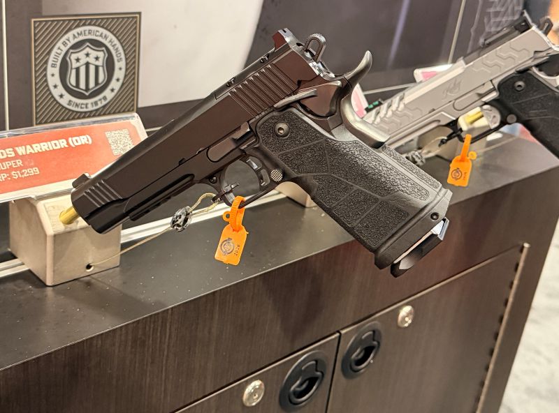 A black 1911 handgun on a wall mount at a gun show, next to other 1911 style pistols. 