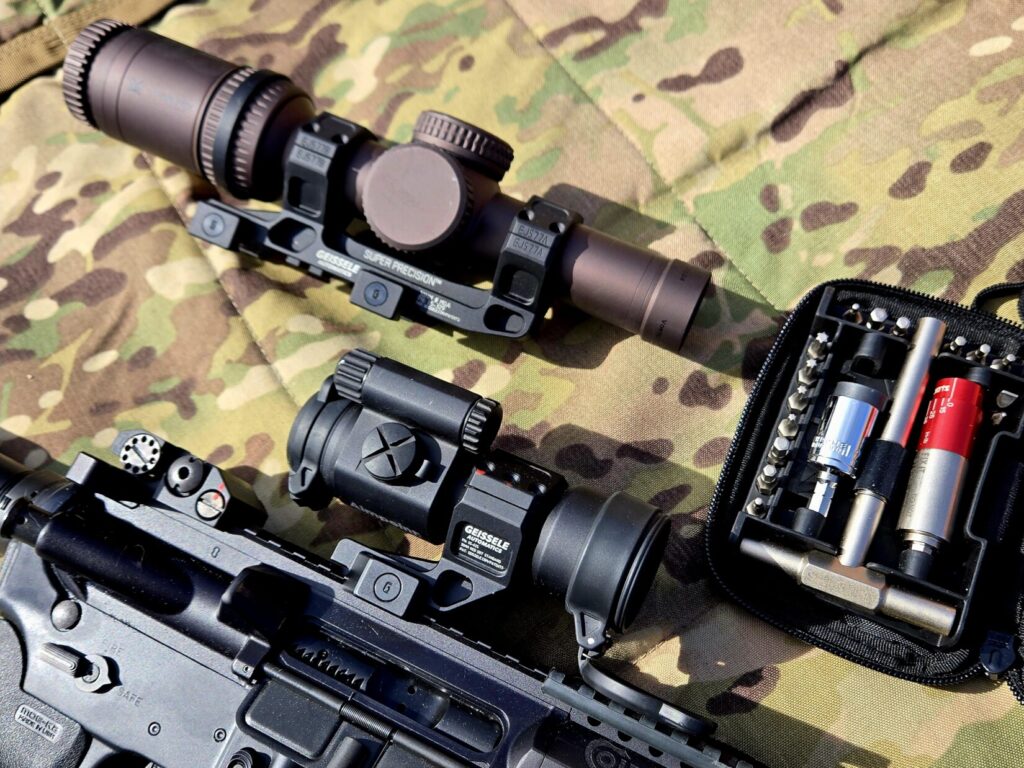 A LPVO optic in a cantilever mount next to a rifle with a red dot and a wrench set against a multicam background