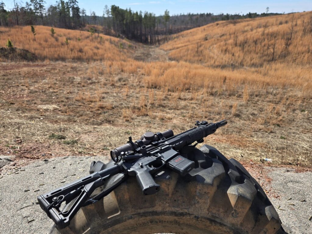 A rifle on a tractor on a tractor tire with an open range in the background