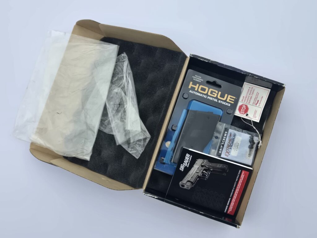 a box with firearm manual spare grips and screws against a white background