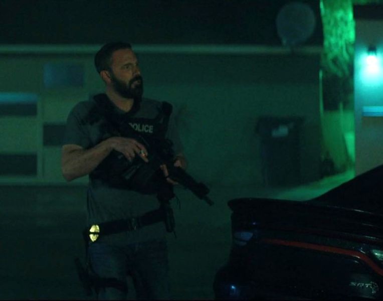 A person in a vest, holding a rifle at low ready with his finger off the trigger.