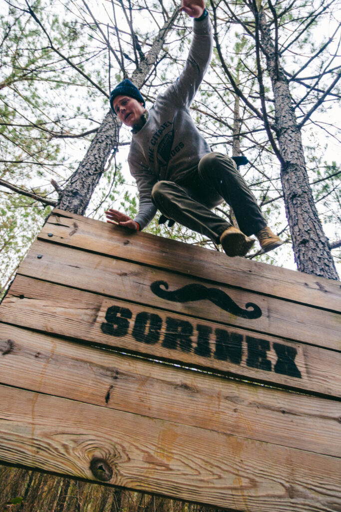 A man climbs over a wooden wall in a pine forest