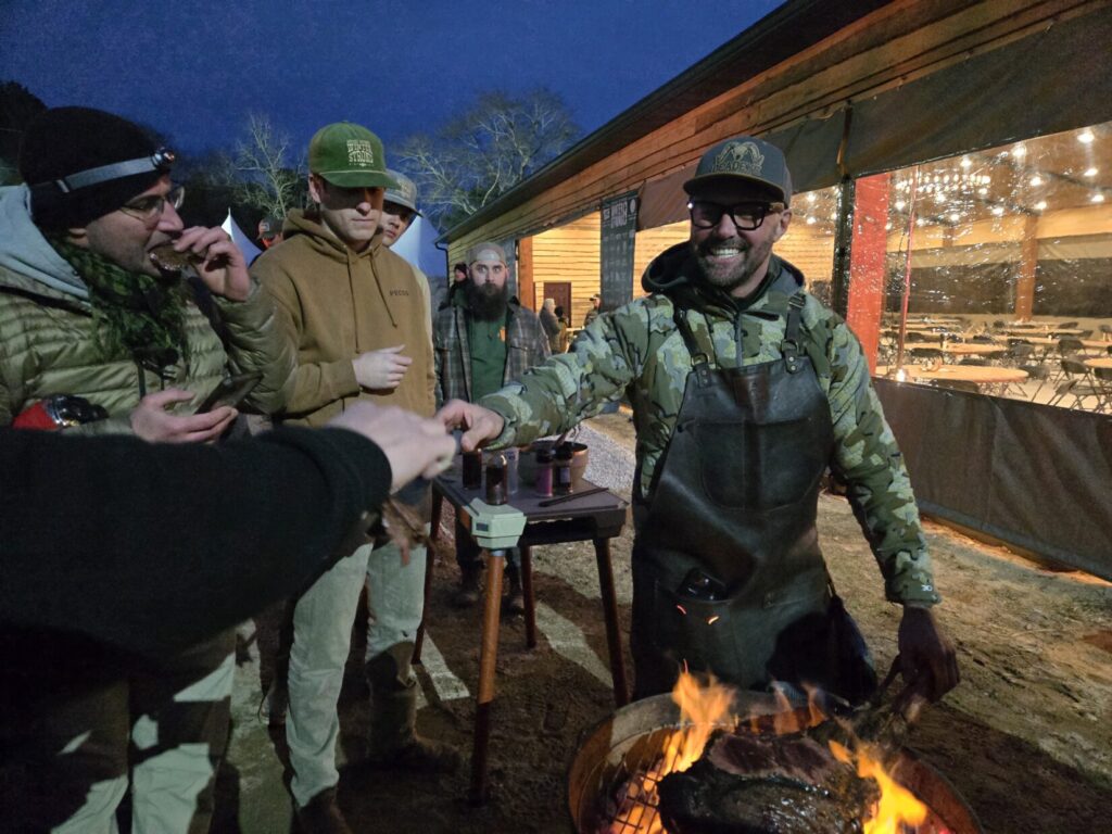 A man stands at a grill serving meat to people nearby