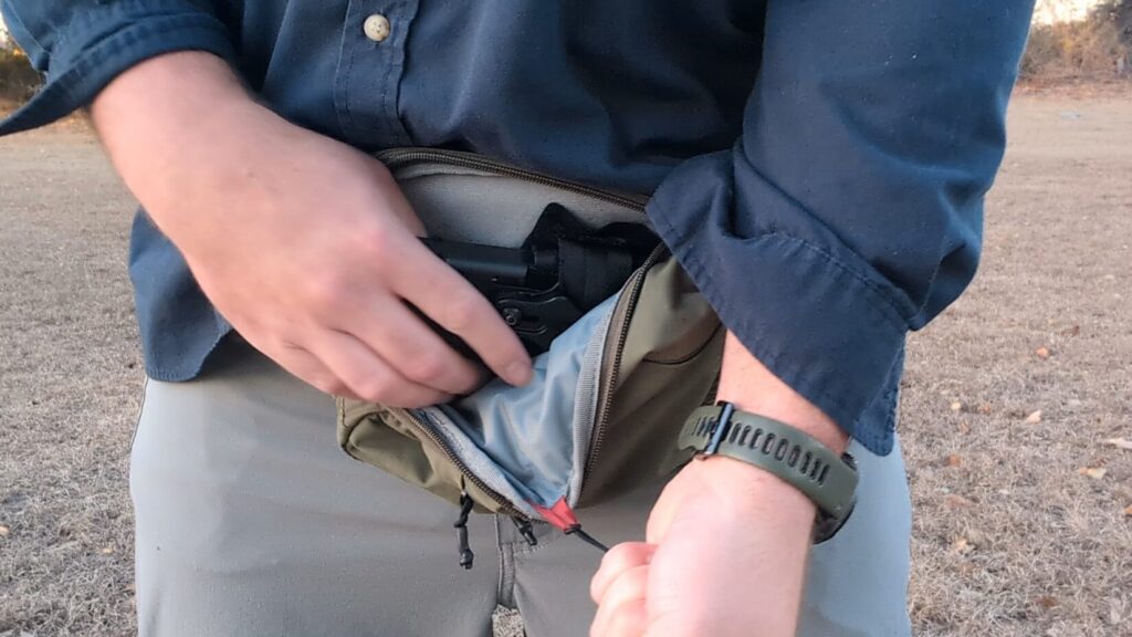 The bag is pulled open by the tab, and the person’s hand reaches inside to grip a concealed handgun.