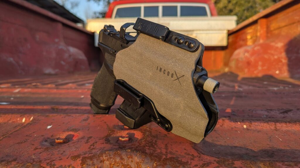 The holstered Echelon standing upright on a weathered red truck tailgate during sunset.