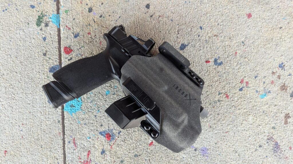 The back side of the holster and firearm laid on concrete, showing the clips and the optic's positioning.