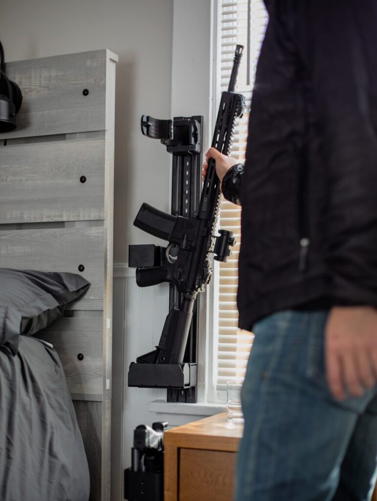 Rifle mounted to a vertical wall rack next to a bed