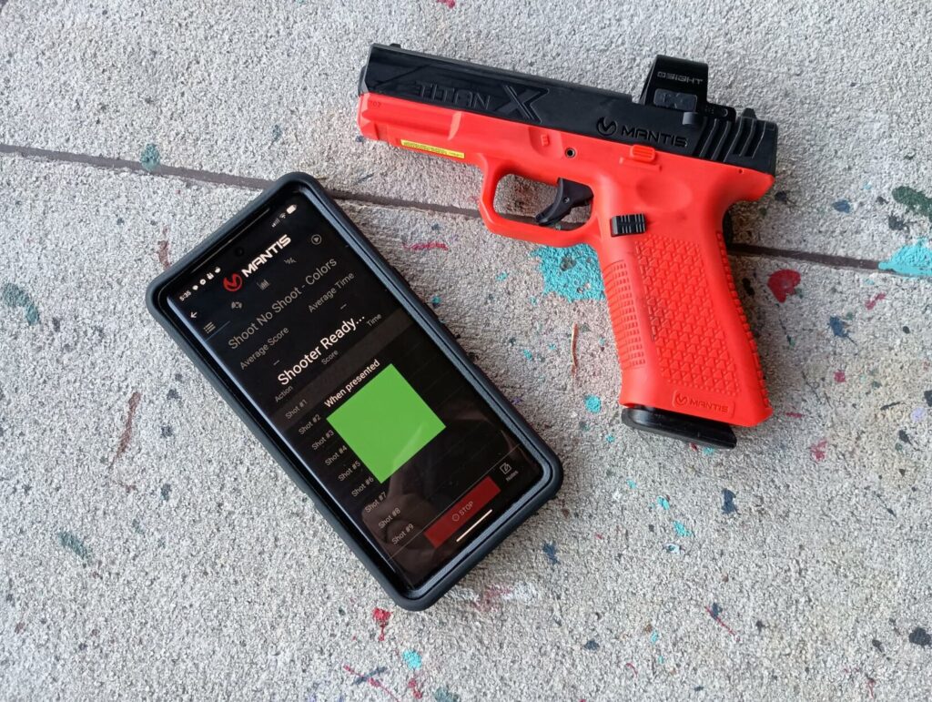 The training pistol next to a smartphone screen glowing bright green, indicating a "Shoot" command during a decision drill.