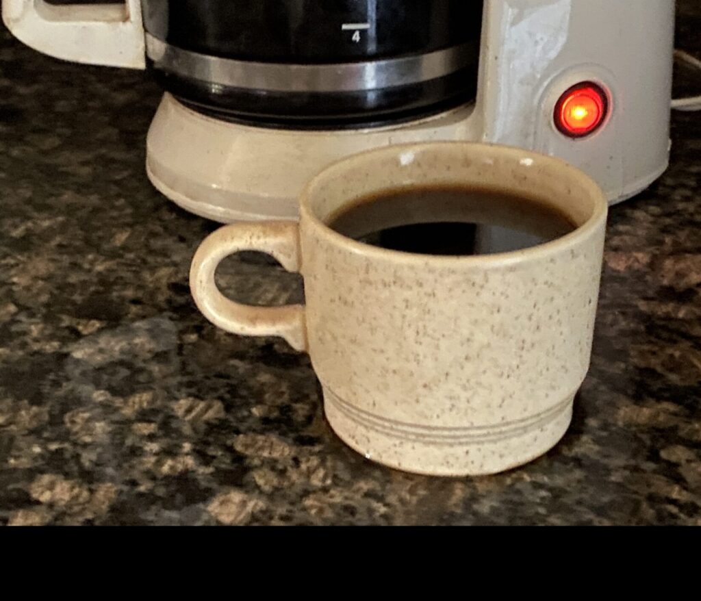 a cup of coffee on a counter with a coffee pot in the background