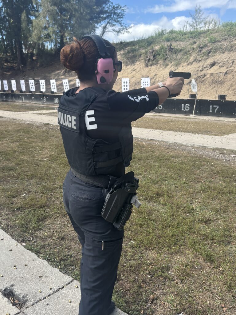 female police officer aiming a handgun downrange. Her holster has the tourniquet pouch attached