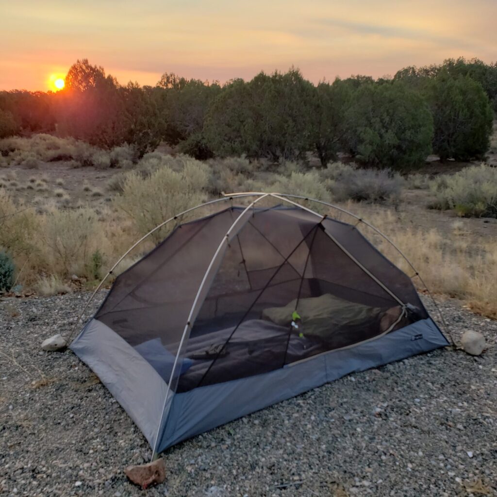 A tent in a desert environment with a sleeping bag and sleeping pad.