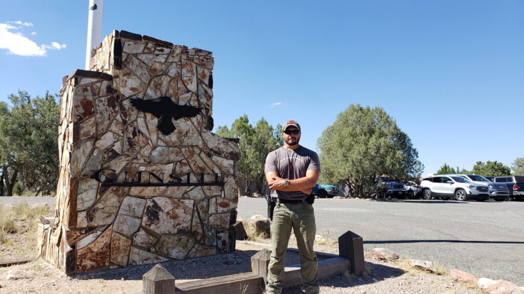 a man standing next to a stone wall with cars in the background