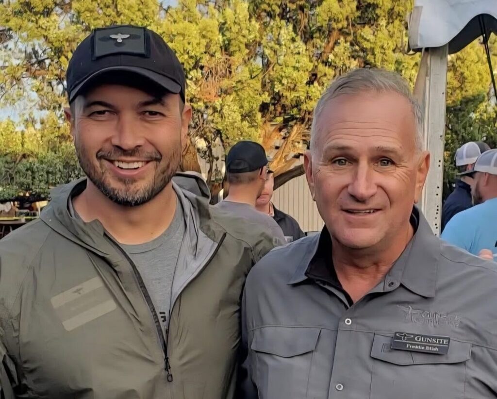 two men smiling for a photo with people in the background
