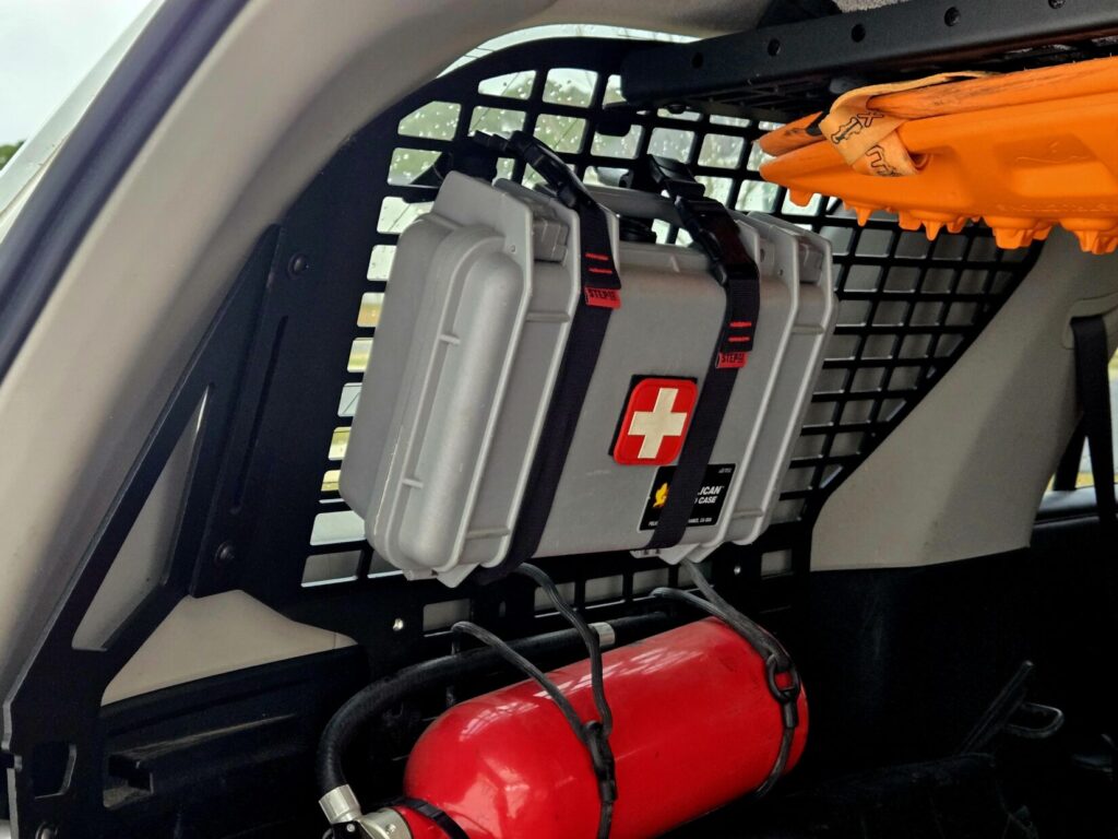 A medical kit strapped to a metal grate with a fire extinguisher and recovery boards