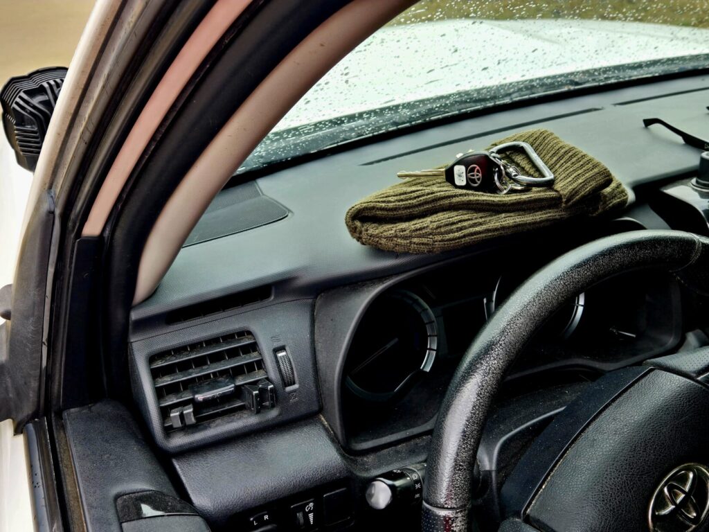 A set of keys on top of a green wool hat on the dashboard of a vehicle