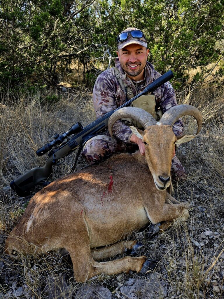 A man in camouflage with an aoudad sheep and bolt action rifle