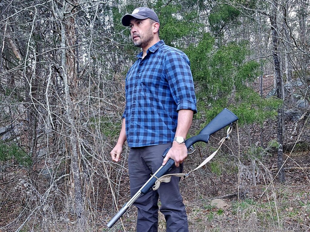 A man holding a rifle at his side with a woodland backdrop