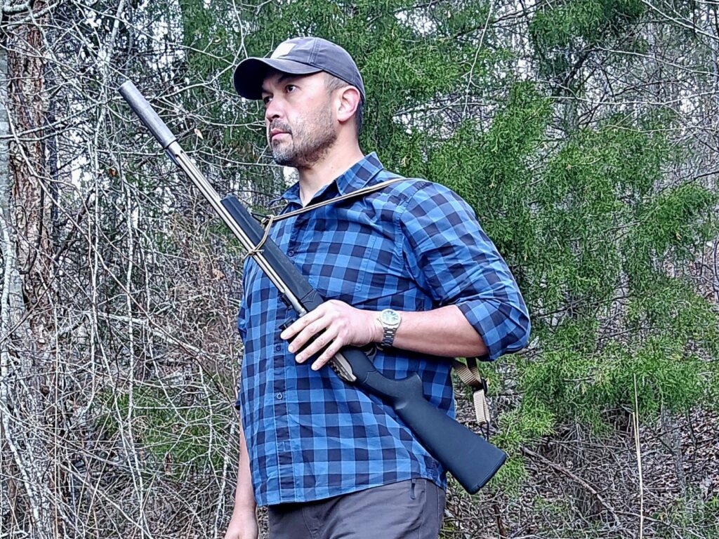 A man holds a rifle in his left hand with the barrel forward