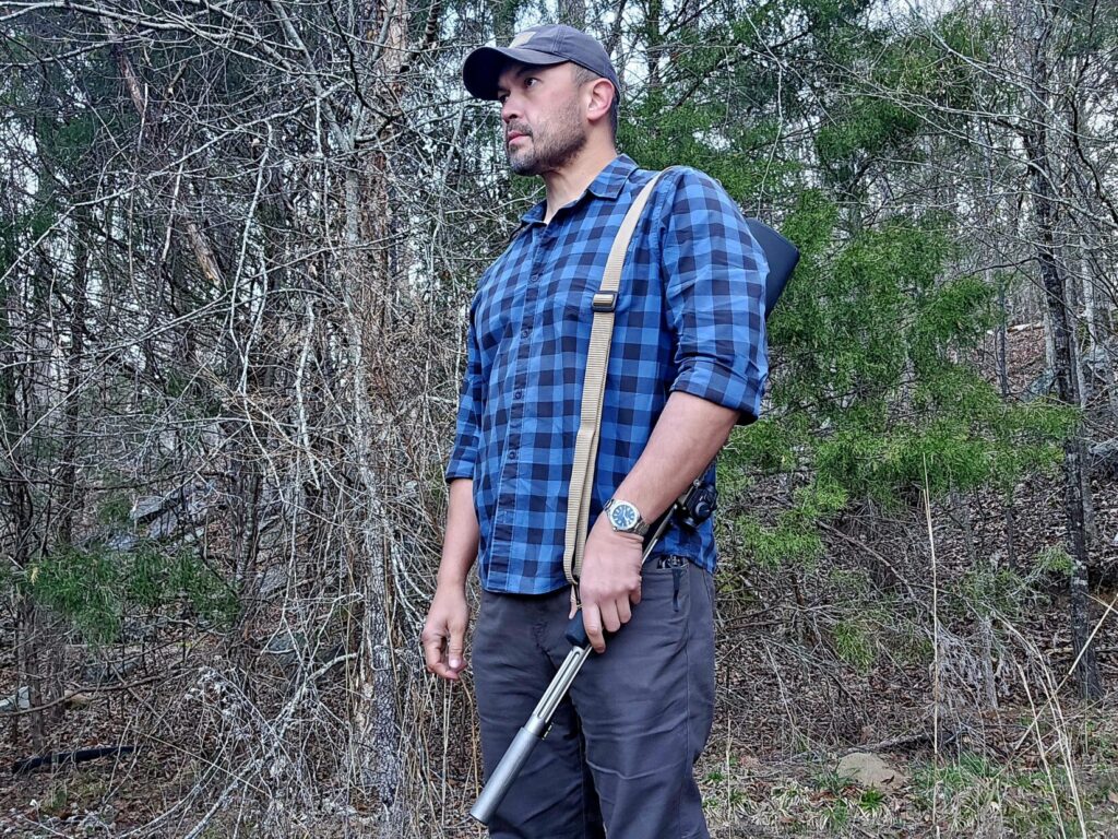 A man in a blue shirt stands with a rifle over his support side