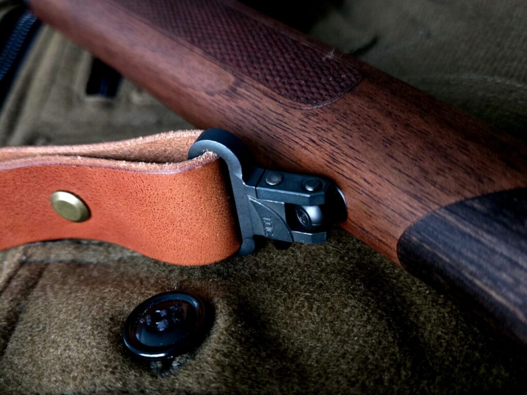 A rifle sling swivel stud on a wooden rifle forend with a wool backdrop