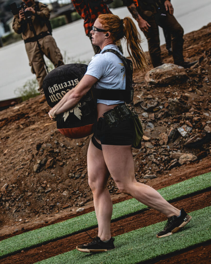 A woman in tactical kit carrying a weighted sand bag.