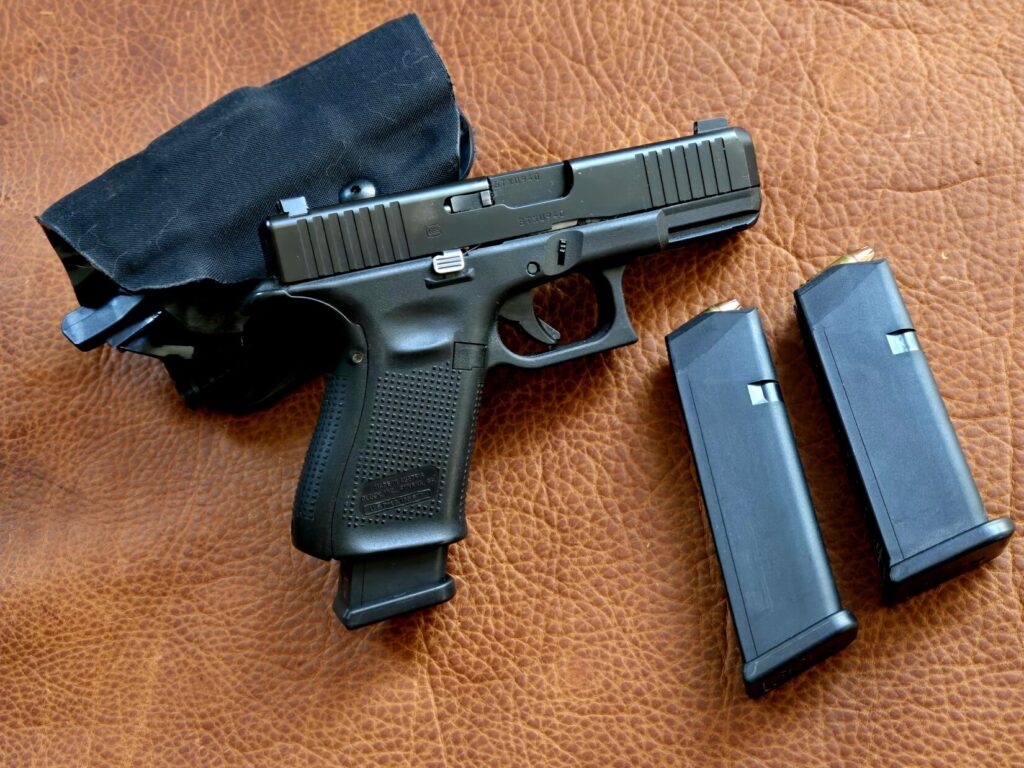 A Glock pistol with holster and multiple magazines against a leather background
