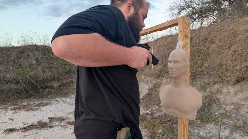 A tight shot of a shooter practicing a facial index push, using their non-firing hand to manipulate the mannequin's head while preparing to fire from a retention position.