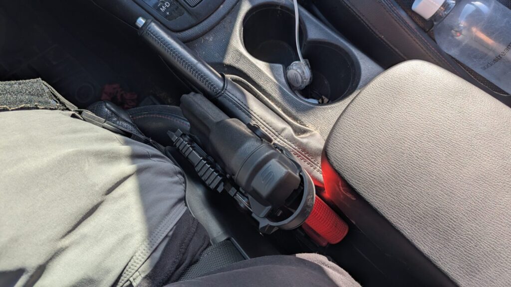 Top-down view of a red training pistol in a holster stuck between the driver's seat and the center console.