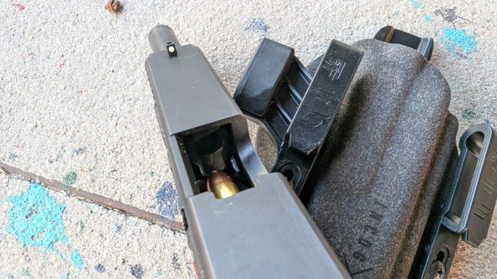 Top-down view into the open ejection port of a pistol, showing a round being fed into the chamber.