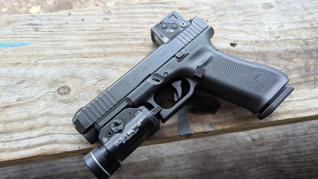 
Top-down profile view of a Glock 47 Gen 5 resting on a wooden bench, showing the Aimpoint COA red dot and Streamlight TLR-1 HL.
