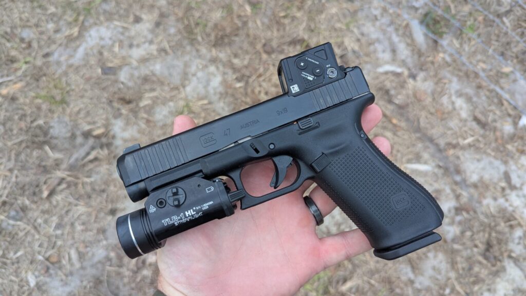 Close-up of a Glock 47 Gen 5 held in hand, showing the "Glock 47" slide markings and the compact Aimpoint COA optic.