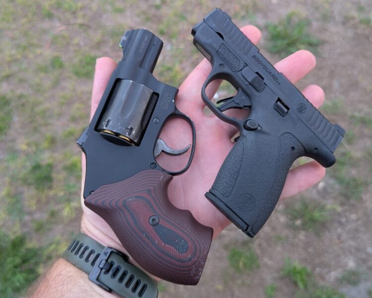 A hand holding a Smith & Wesson snub-nosed revolver with wood-patterned grips above a Smith & Wesson Bodyguard 2.0 semi-automatic pistol for a size comparison.
