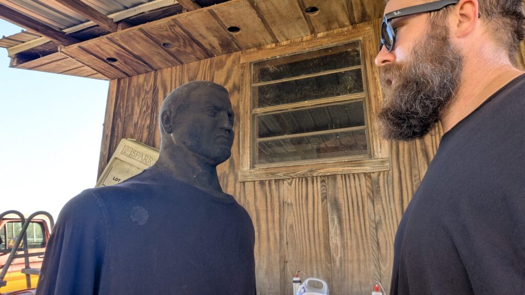 A close-up profile of a bearded man in sunglasses staring intently at a training dummy, illustrating target fixation and aggressive posturing.