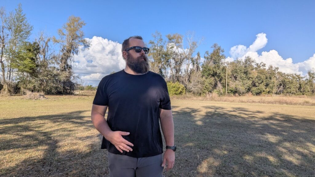 A man subtly touching or adjusting the front of his waistband with his left hand, demonstrating a "security pump" to check a concealed item.